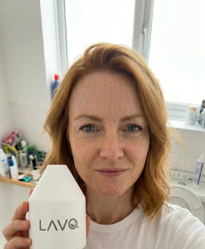 Ginger woman holding LAVO Pod in her bathroom, behind her a window